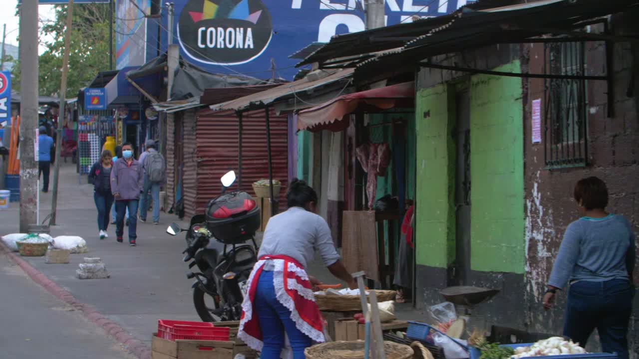 Slow motion street view of people walking sidewalk, colorful stores, street vendors selling fruits, someone sweeping in Zone 18 Guatemala City - Handheld footage