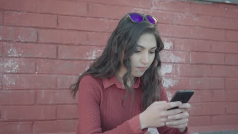 girl texting with the smartphone with brick wall in the background, pan