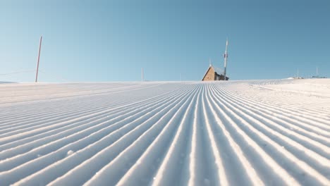 lateral shot of freshly groomed snow with a distant mountain cabin under a clear blue sky in andorra.
