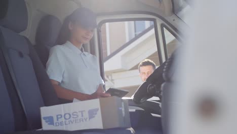 female postal service courier sitting in mail van and delivering package to man