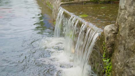 Small man-made waterfall in Padang Panjang, West Sumatra, Indonesia, near the brightly colored boats, showcasing a blend of natural and human-made elements.