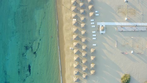 Top-down-view-Pristine-water-beach-shore-with-umbrellas-on-sand,-Milopotas-Beach