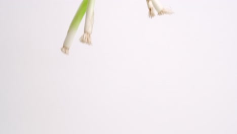 Whole-green-onions-raining-down-on-white-backdrop-in-slow-motion