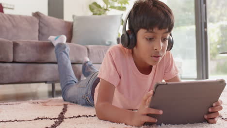 boy wearing headphones lying on floor using tablet, smiling and enjoying