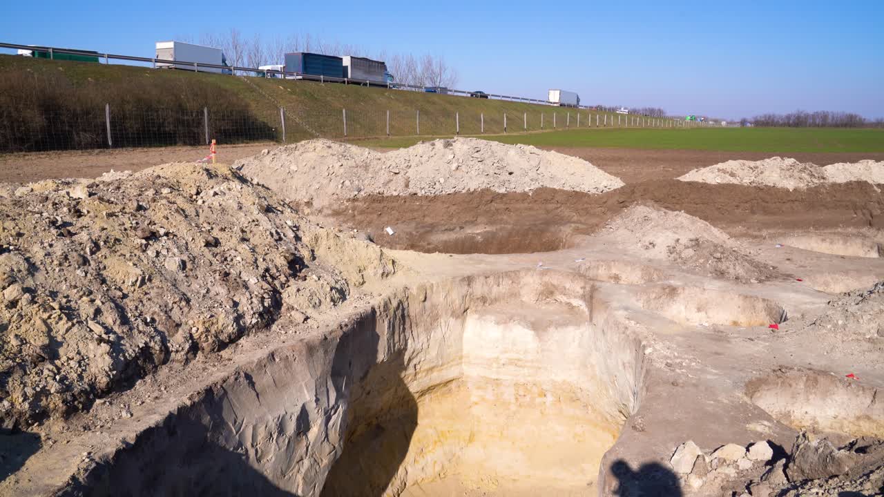 High angle tilt down looking into pit at archaeology site. Highway traffic in background