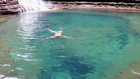 joven nadando en agua azul clara de cascada desde el ángulo superior