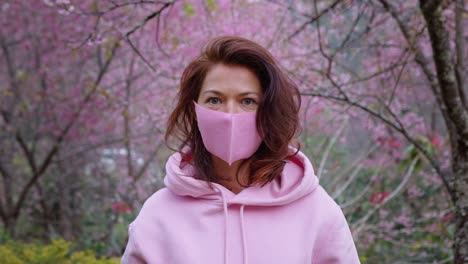 woman wearing pink mask in pink cherry blossom trees