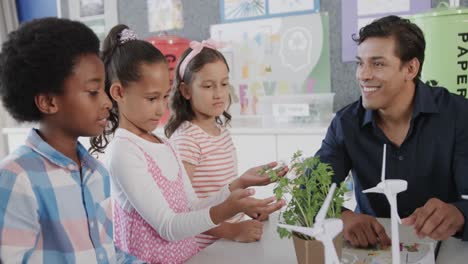 diverse male teacher and children with plants and turbines in elementary school class, slow motion