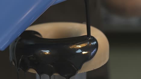 confectioner pours chocolate topping on big baked doughnut