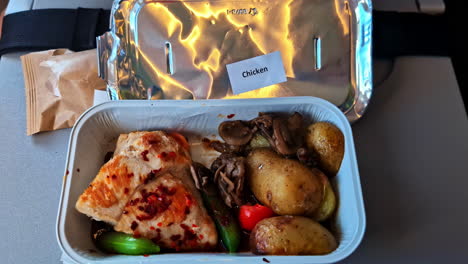 airline meal with chicken, potatoes and vegetables served in foil tray on flight tray table