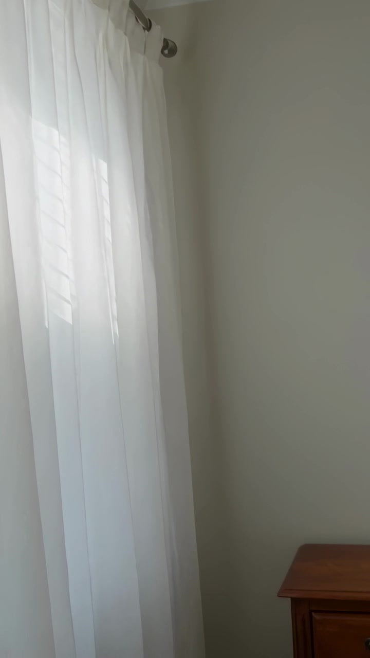 Video verticale: La telecamera inizia dall'angolo della camera da letto, panoramica a destra mostrando tende trasparenti, persiane e un tavolo.