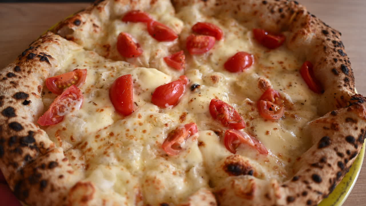 Primo piano di pizza appena sfornata, guarnita con formaggio fuso e pomodorini