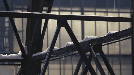 Close-up-of-a-metal-triangular-structure-covered-with-snow-that-is-melting-and-water-is-dripping