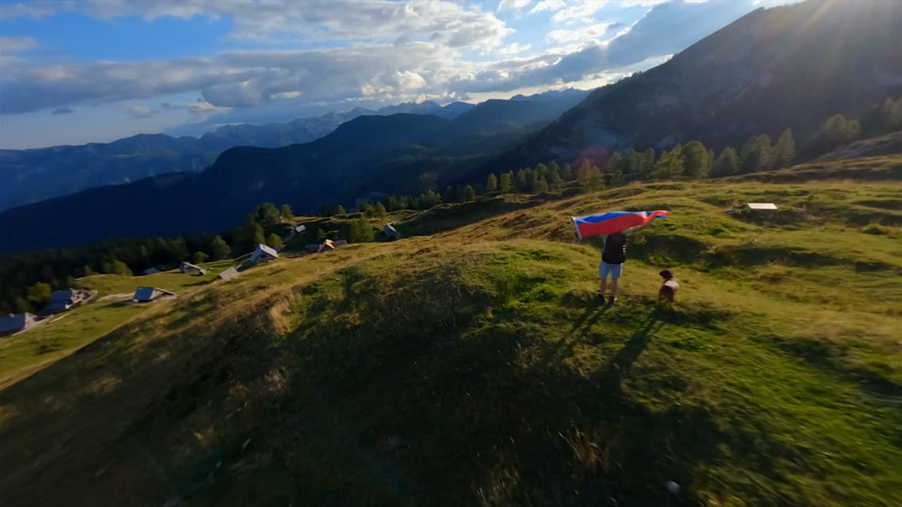 las imágenes de fpv se filmaron en el pueblo de montaña esloveno en los alpes con un dron volando rápido sobre las montañas filmadas con una gopro con increíbles paisajes circundantes con un excursionista sosteniendo una bandera