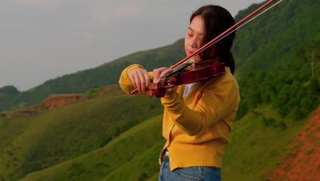 slow motion of woman playing violin in nature, green hills in background