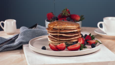 super slow motion powdered sugar is being sprinkled over the pancakes pile, served with blueberries and strawberries. healthy tasty traditional breakfast. shot with high speed cinema camera