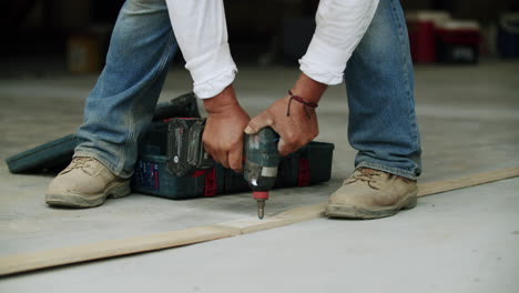 a person using a power drill to secure a screw into a wooden plank on the ground