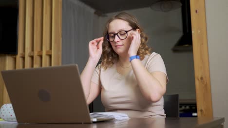 woman is sitting at desk, she puts on her glasses and starts working. the beginning of the working day. e-learning, remote work on a laptop via the internet, work at home, distance, pandemic