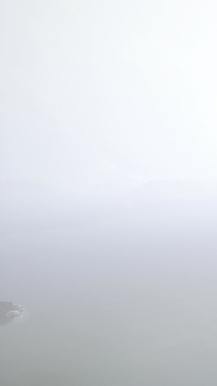 Fog covers the coastline and mountains near the sea in a gray sky