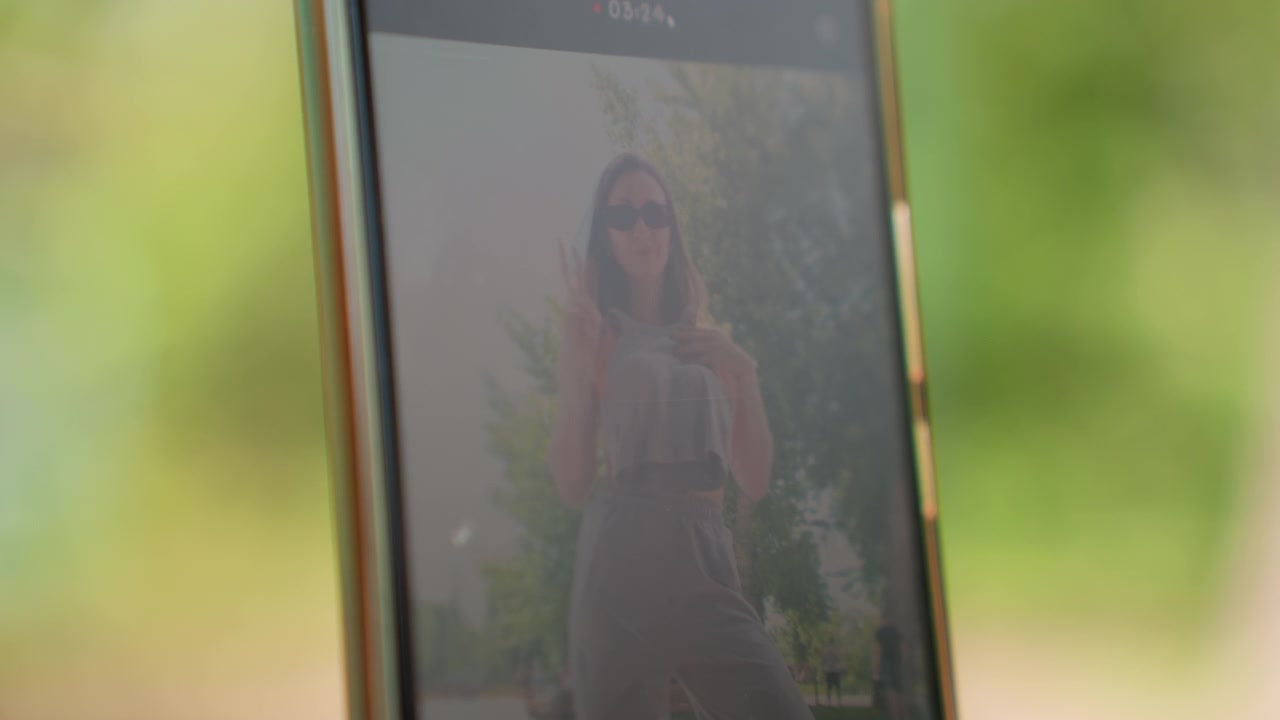 Close up of woman posing outdoors on her smartphone screen changing hand gestures and outfits. Woman holds different items like folded clothes or makes peace signs against urban park