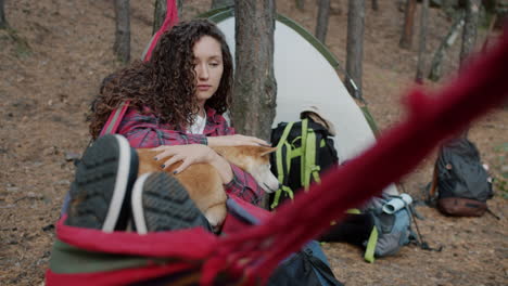 woman relaxing in a hammock with her dog while camping in the forest
