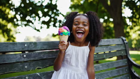 a happy young girl enjoys a rainbow ice cream cone in the park