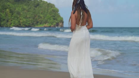 descending camera movement of a young lady in a white dress walking on the beach