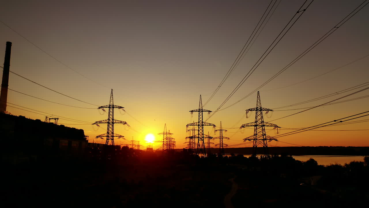 Voltage high electric lines at sunset. Electricity pylons at dusk against orange sun. Silhouette of steel electric towers in the evening.