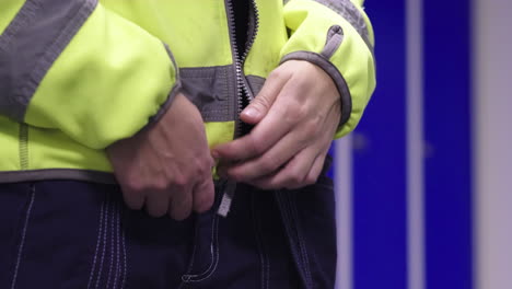 Close-up-wood-worker-zipping-up-his-reflective-jacket-in-locker-room-before-work,-emphasizing-importance-of-safety-gear-in-logging-forestry-industry-as-he-prepares-for-his-shift-at-wood-mass-facility