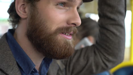 young bearded man wearing beret in the urban bus while looking at his smartphone