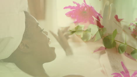 animation of pink flowers over happy african american woman relaxing in bathtub