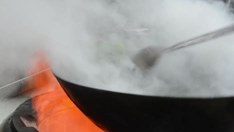 chef cooking stir fried dish in wok - close up