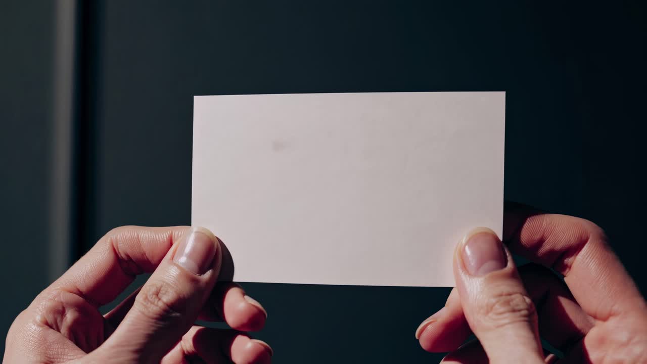 Primo piano di mani che reggono un biglietto vuoto su uno sfondo scuro, suggerendo un concetto video