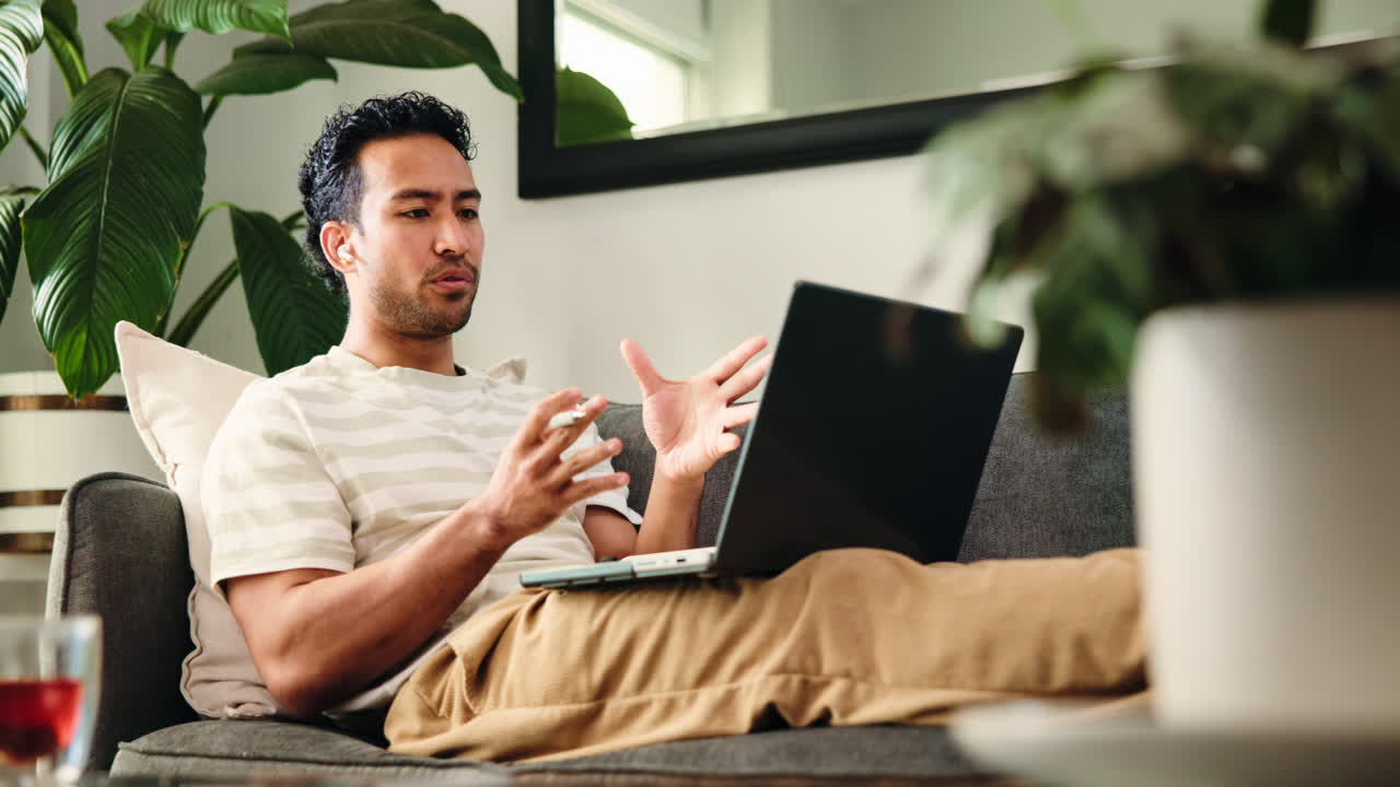 Young Man Talking and Working on Laptop from Home Couch