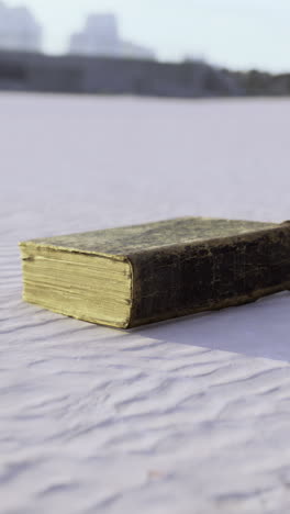 weathered book lies alone on a textured sandy surface