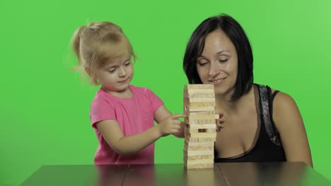 mother and daughter plays block removal game. pulls wooden blocks from tower