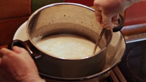 Looking-down-at-a-boiled-milk-icing-in-a-saucepan-in-a-bain-marie,-stirred-with-a-metal-spoon