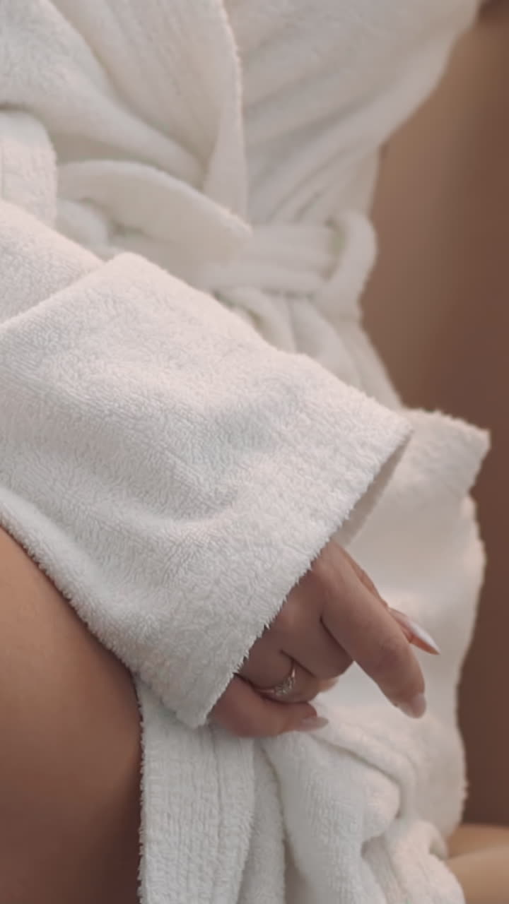 Slim woman wearing long white gown sits in armchair baring knee in spa salon extreme closeup. Beauty and healthcare procedures undergoing. Hotel service
