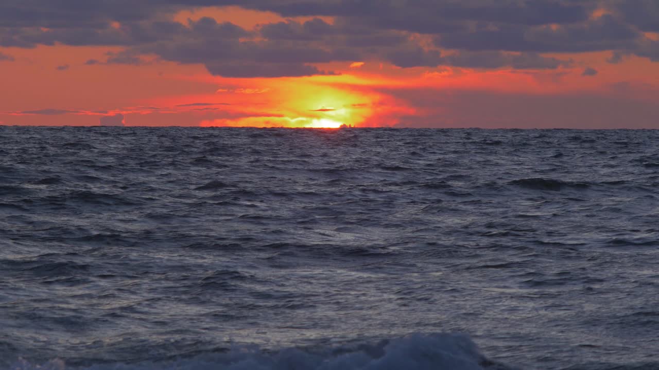 romántica puesta de sol roja escénica vibrante sobre la playa báltica en liepaja con nubes azules vibrantes, plano general