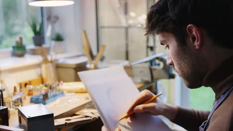 close up of male jeweller sketching out design for ring in studio