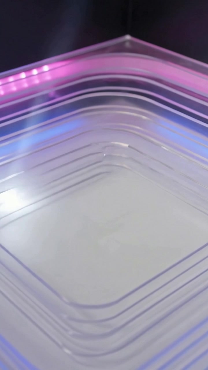 Video verticale: LED pulsanti, vassoi impilati proiettano un bordo rosa-blu su superficie lucida, evidenziando le scanalature.