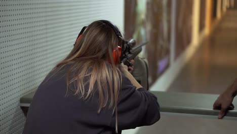 mujer con rifle neumático en las manos en el campo de tiro con objetivo, emocionada y sorprendida por el disparo