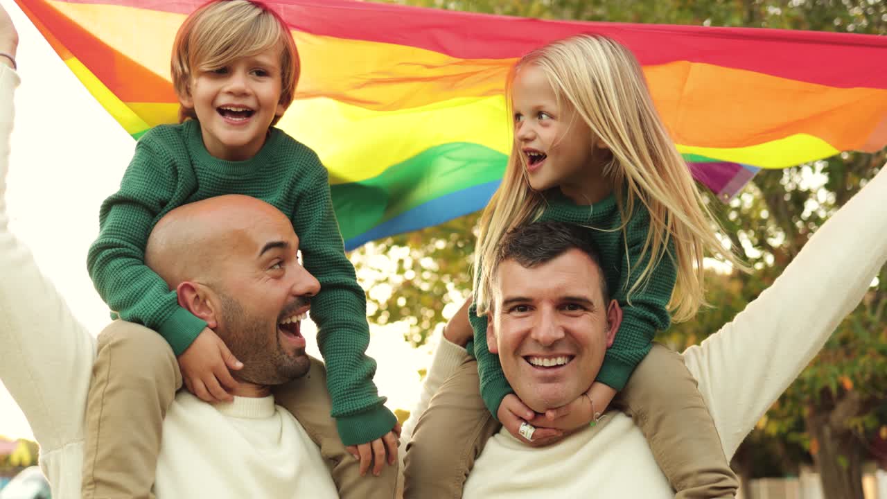 una pareja gay con hijos se divierten sosteniendo la bandera del arco iris lgbt al aire libre en el parque de la ciudad - concepto de familia y amor