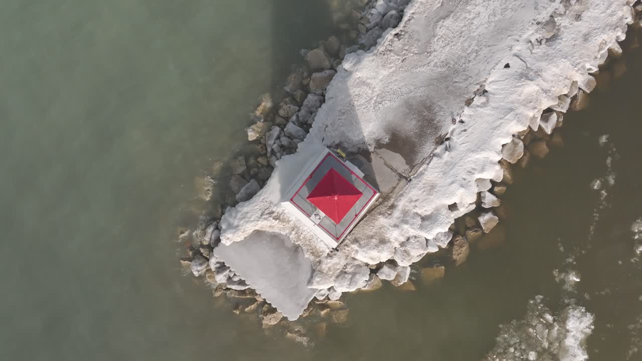 Aerial shot of a vibrant red hut on a snowy Southampton pier, waterside rocks visible, winter season, isolated structure