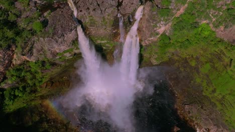 capturing an aerial view of a stunning waterfall cascading into a rocky gorge, creating a rainbow amidst the lush green cerrado of chapada dos veadeiros national park, brazil, slow motion drone shot