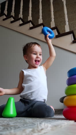 active energetic caucasian toddler runs up to toy pyramid. joyful kid stacks rings on the base. low angle view.