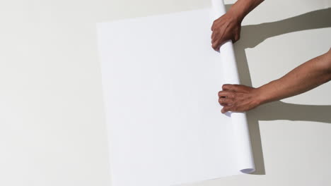 video of hands of african american man with rolling up white paper on white background