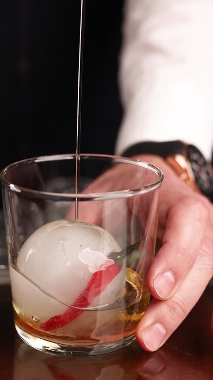 Bartender preparing an iced whiskey cocktail with a chili pepper garnish