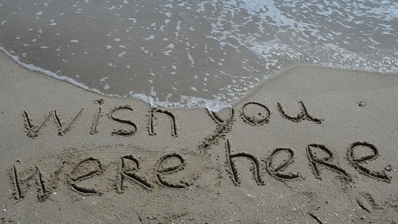Conceptual wish you were here text handwritten in sand on a beach . Shooting on the beach