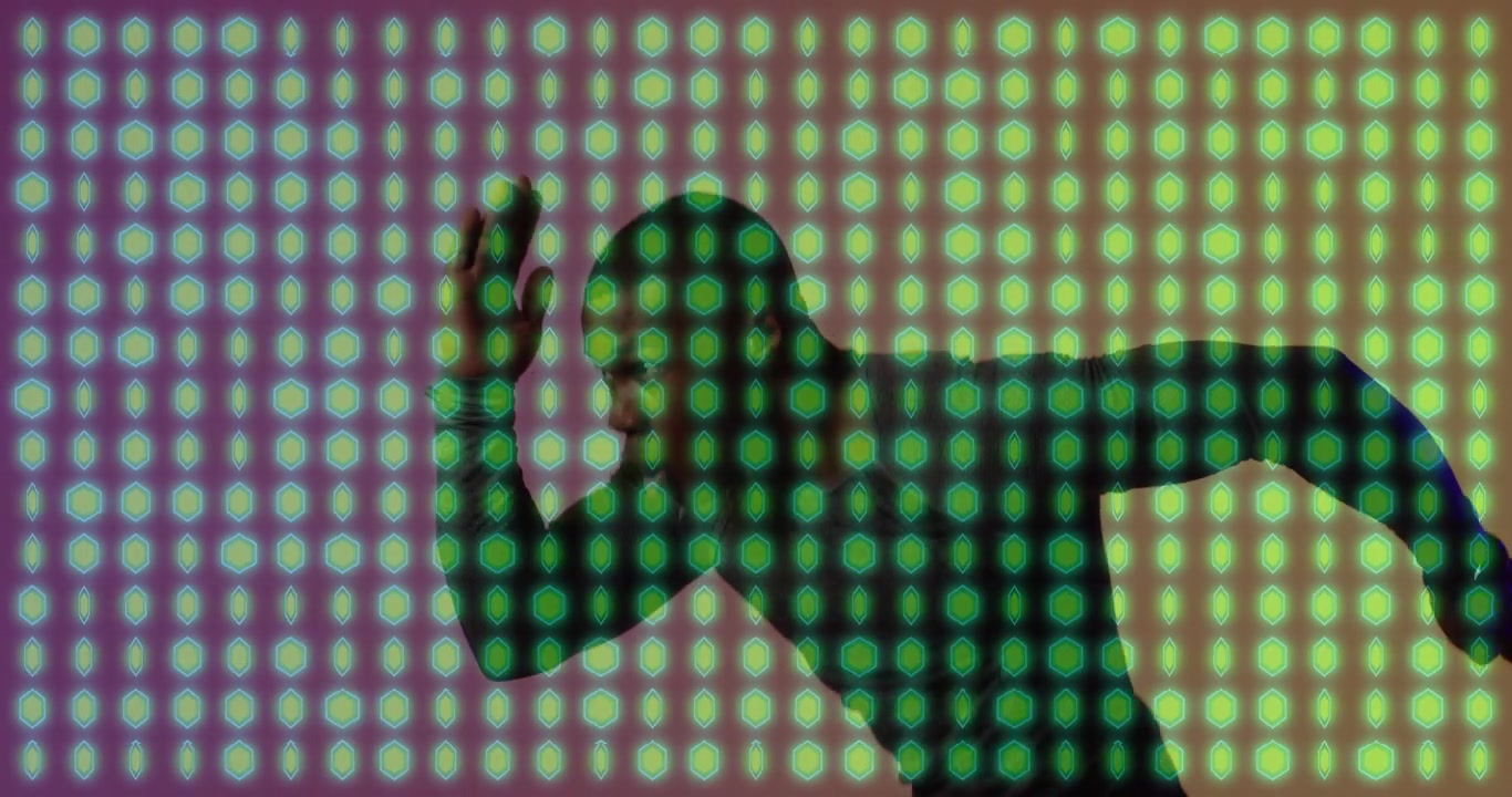 Un performer uomo alza il braccio in posizione di partenza, mostrando un movimento dinamico in un ambiente tecnologico su una griglia LED mutevole.